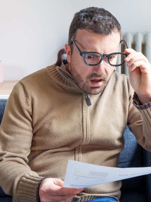 Shocked man reading some bills energy expenses on sofa living room